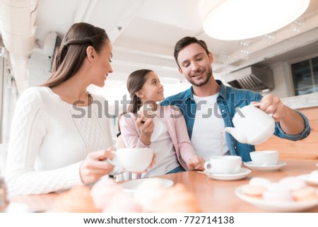A young family came together in a cafe. Mom, dad and little daughter drink tea, eat cakes. They are happy together.