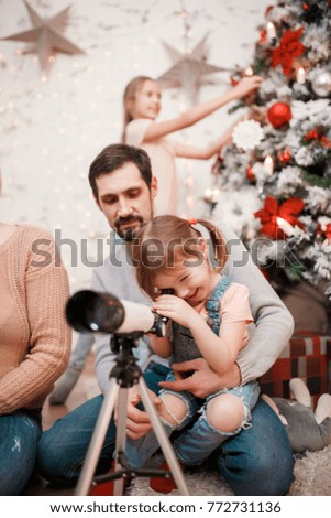 Image of parents and daughters with telescope on background of decorated New Year's fir