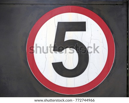 The speed limit sign is five, attached to a black metal panel.