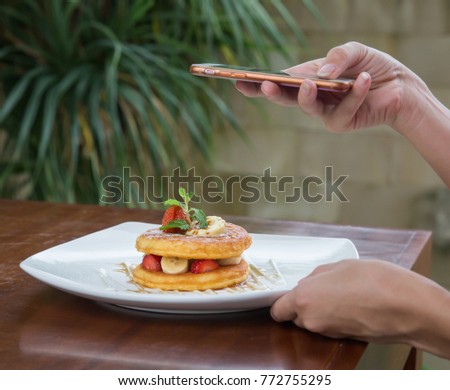 Pancake with banana and strawberry. Young girl takes picture with her phone