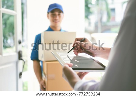 delivery, mail, people and shipping concept.Young woman sign in digital mobile phone after receiving parcel from courier at home. Royalty-Free Stock Photo #772759234