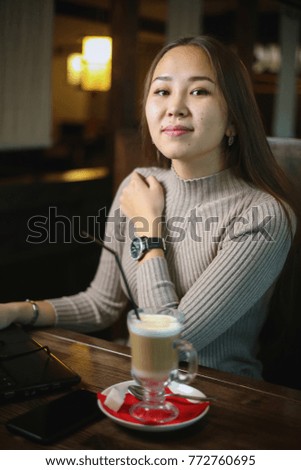 Beautiful Asian girl sitting at cafe with laptop and drinking aromatic coffee