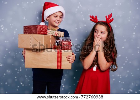 Happy siblings with stack of gifts among snow falling 