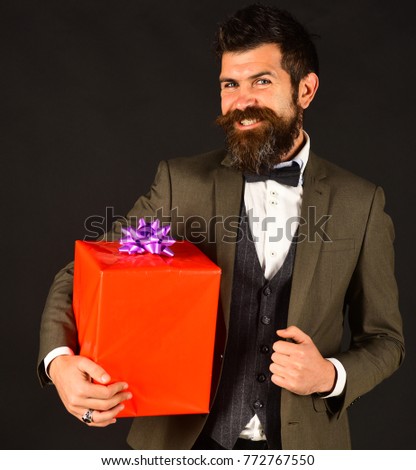 Businessman with happy smiling face and red gift box on brown background. Macho in retro suit presents wrapped gift. New year gift concept. Man with beard holds present.