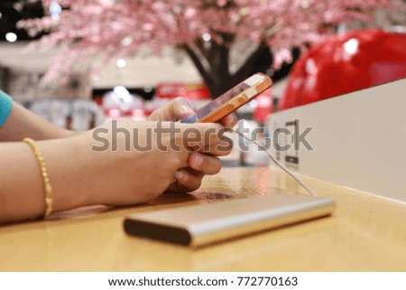 hands of a women playing a smartphone on wooden table in the blur shopping mall background.