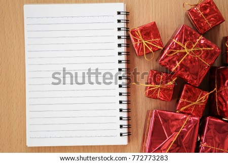 Empty notebook placed near the red gift box on a brown wooden floor and have copy space to input ideas of your work.