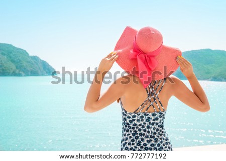Back view of model in straw hat posing on background of lagoon of resort hotel among mountains. 
