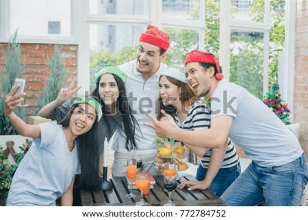 Group young people having drink and fun in santa hats throwing colorful on celebrating new year or christmas party, taking selfie by smartphone, exchanging presents, happy time 
