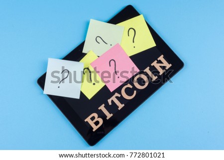 Word bitcoin in abstract letters and question questions on stickers glued to the tablet.