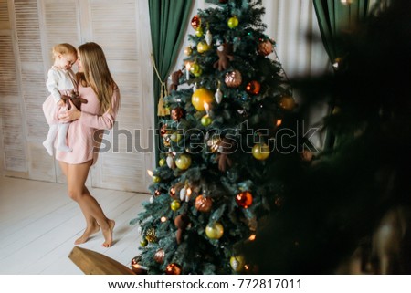 Photoshoot of a young mother with her daughter at the Christmas tree for the New Year.