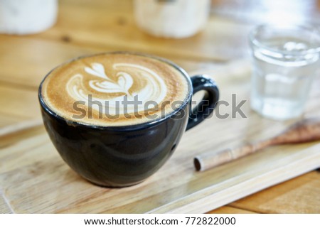 a cup of coffee latte art on the wooden tray with blurred glass of water