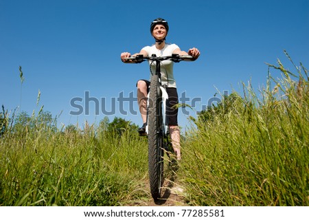 sport and recreation conceptual photo of Young sporty girl riding a bike on a field path - offroad with clear blue sky in background