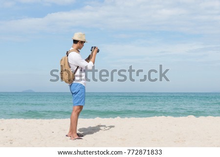 Young Asian man traveler look at his vintage camera, Happy male photographer on the beach, summer holiday and vacation lifestyle concepts