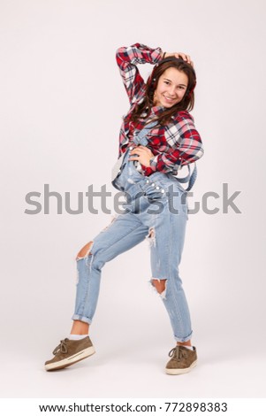 A girl with an outstretched leg holds on to the headphones, looks straight on a gray background