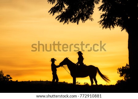 Silhouette of cowgirl and cowboy riding a horse.
