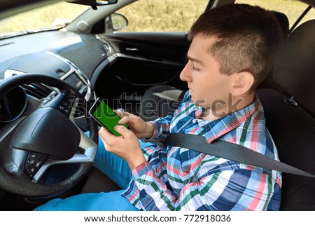 Young man driver using smart phone in car. Driver sitting in car and holding mobile smart phone with isolated screen. Modern smartphone with blank screen, copy space for text or design