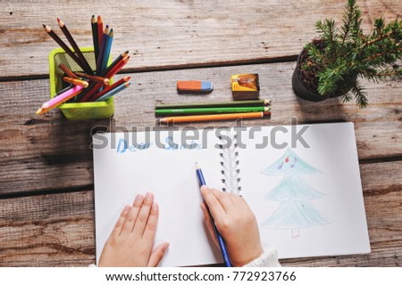 Preparing for the Christmas holidays. girl writing a letter to santa, wooden background, top view of copy space, female hands in picture