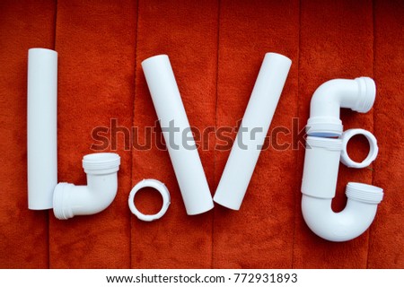 The inscription love is made up of white, plumbing, plastic pipes, fittings, flanges, rubber gaskets on the background of a red carpet. A word of love written by water pipes.