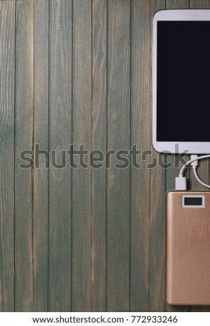 Portable power bank and tablet PC on wooden background. Flat top view. Space for text. Vertical photo


