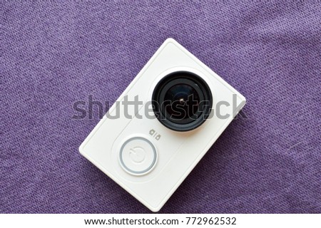 White action camera with a large black lens on a violet background