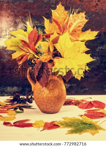 Clay jug with autumn leaves and wheat on white wooden desk. Thanksgiving day and autumn concept