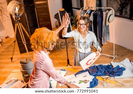 Two female multi-ethnic fashion designers working with clothes and drawings at the studiowith different tailoring tools