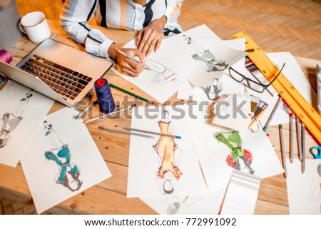 Fasion designer sketching clothes drawings at the table with tailoring tools and laptop Royalty-Free Stock Photo #772991092