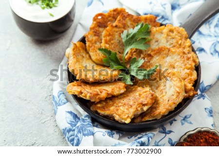 Potato latkes traditional jewish pancakes with sour cream, parsley, dry red pepper flakes and mint sauce. Background, white napkin with blue flowers. Hannukah celebration dish concept. Close up.