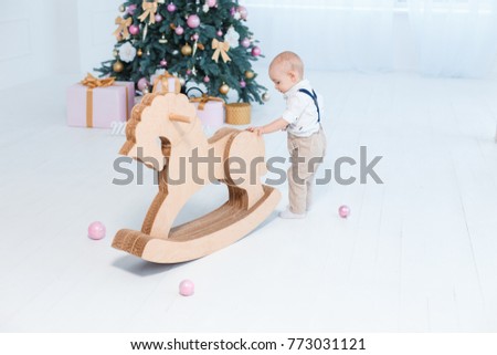 little boy is playing with a cardboard horse against the backdrop of a Christmas tree.