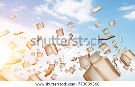Man in white clothing keeping eyes closed and looking concentrated while meditating among flying books in the air with cloudy skyscape on background.
