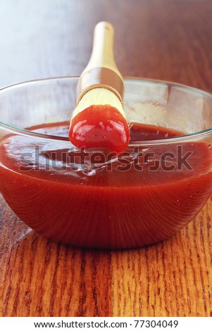 Basting brush and bowl of tangy barbecue sauce on an old battered wooden table with extreme shallow depth of field.