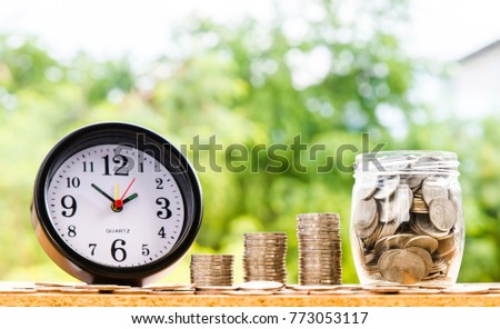 alarm clock and step of coins stacks and coins in jar, nature background, money, saving and investment or family planning concept, over sun flare silhouette tone.