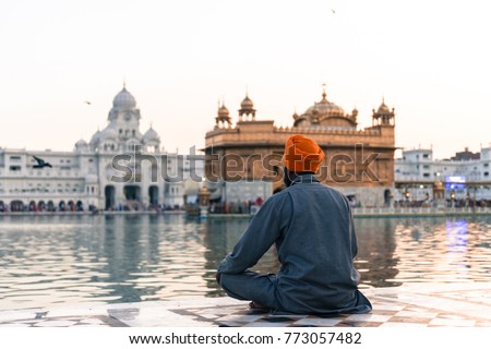 Wide angle picture of Indian man wearing orange turban praying in front of the holy lake at Sri Harmandir Sahib, known as Golden Temple, site of Sikhism, located in Amritsar, Punjab, India.