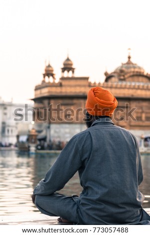 Vertical picture of Indian man wearing orange turban praying in front of the holy lake at Sri Harmandir Sahib, known as Golden Temple, site of Sikhism, located in Amritsar, Punjab, India.
