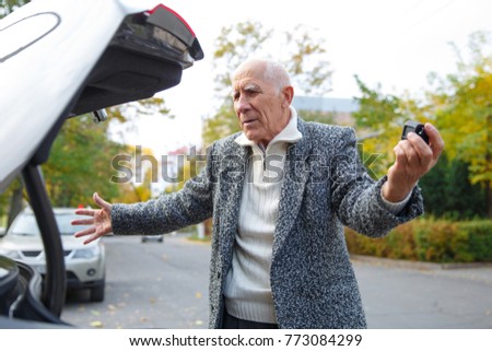 The old man near the trunk of the car, disappointed with his hands.