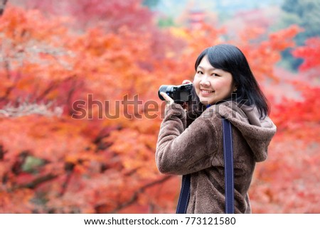 Pretty asian woman on wear winter cloth holding camera with beautiful autumn leave trees on background in japan.