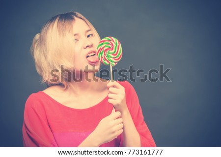 blonde girl teenager in a red blouse licks the lollipop  on a gray background. Toned