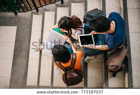 A group of young or teen Asian student in university smiling and reading the book and look at the tablet or laptop computer in summer holiday. Royalty-Free Stock Photo #773187037