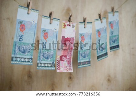 Malaysian fifty ringgit and Indonesian one hundred thousand rupiah banknotes hanging from a clothesline concept for money laundering. Image contain certain grain or noise and selective focus.