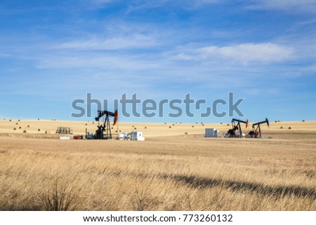 Oil pump jacks in the middle of farm land with hey barrels. Landscape. Oil industry equipment. Calgary, Alberta, Canada. 