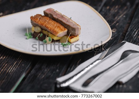 Duck fillet with polenta on irregular shape plate on dark wood background
