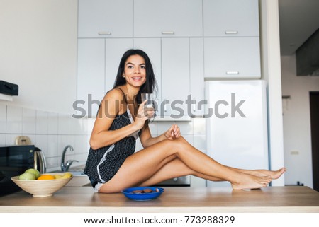 young attractive woman at kitchen in morning, having breakfast, smiling, natural look, drinking milk, looking forward, thinkig