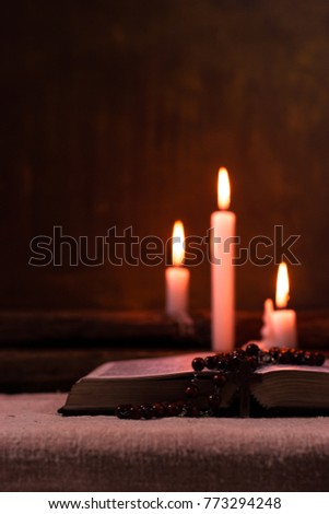 Bible crucifix and beads with a candle on a old oak wooden table.  Beautiful gold background.Religion concept.