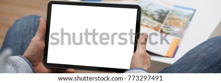 Male hand holds tablet pad in home setting while sitting on the couch engaged an internet surfing using application to press a finger on the display leisure listering music concept closeup. Royalty-Free Stock Photo #773297491