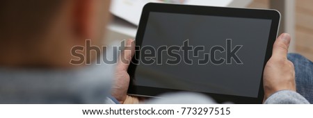 Male hand holds tablet pad in home setting while sitting on the couch engaged an internet surfing using application to press a finger on the display leisure listering music concept closeup. Royalty-Free Stock Photo #773297515