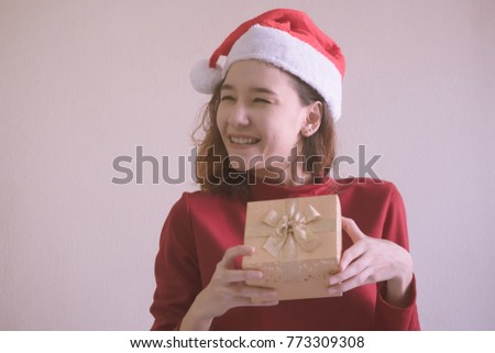 Happy Asian woman dressed in red Christmas hat holding gift box.