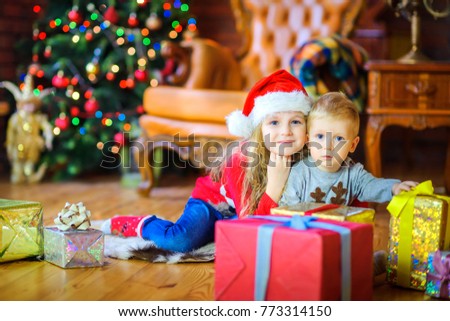 sister gently hugs her little brother sitting on the floor near the gifts
