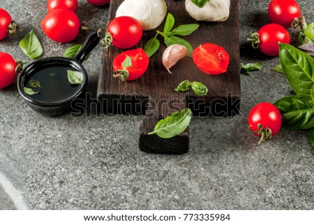 Farm raw organic products. Cooking of dinner in Italian style. Ingredients for caprese salad, pasta, pizza. Basil, tomatoes, mozzarella cheese, olive oil. dark grey stone table. Copy space 