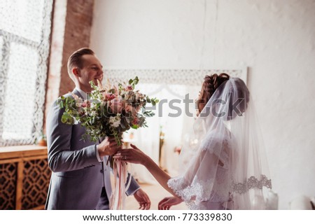 The first meeting. The groom comes into the room to the bride with a bouquet. Pink wedding dress, gray suit and stylish bouquet. Room in the style of Morocco.