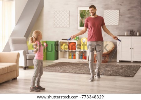 Cute girl and her father jumping rope at home Royalty-Free Stock Photo #773348329